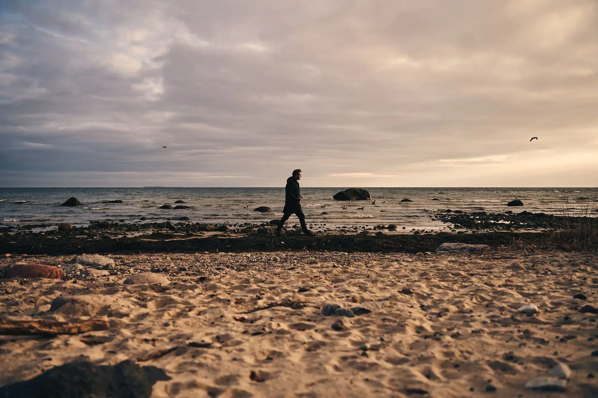 A person walking on a beach at sunset, with clouds in the sky and the ocean in the background.