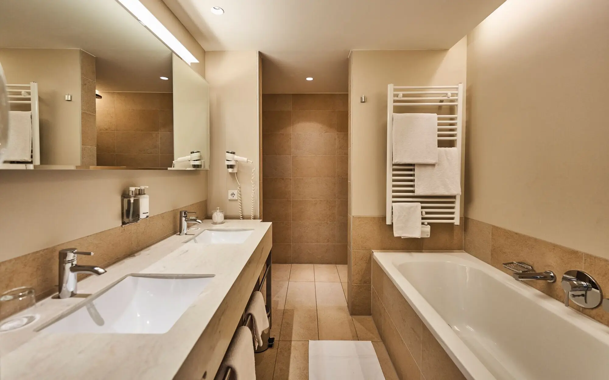 Bathroom with bathtub, shower and washbasin, tiled and with modern fittings.