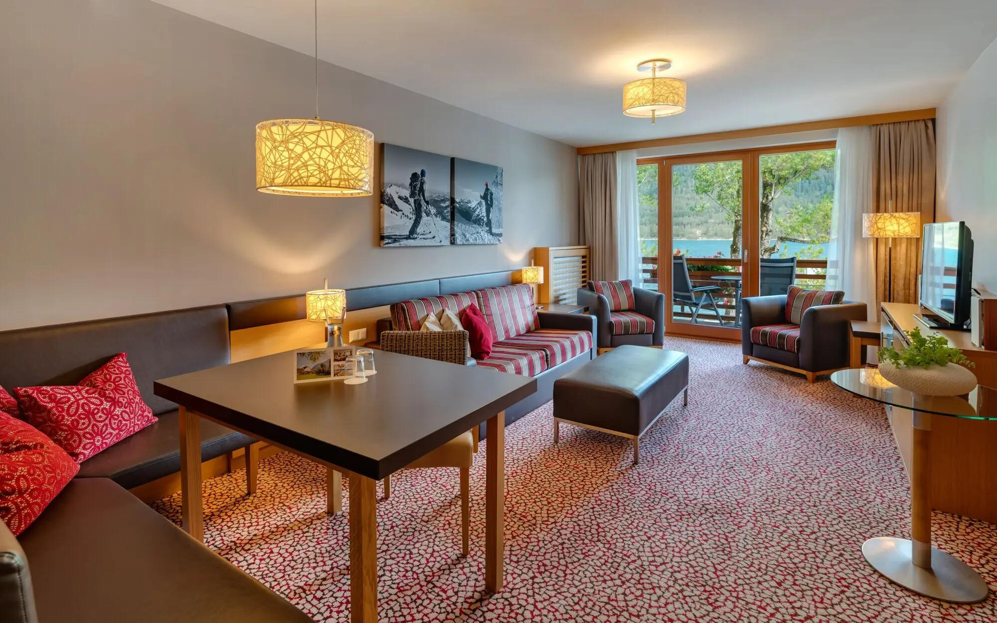 Living room with table, chairs, a sofa and a balcony in the background with a view of Lake Achensee.