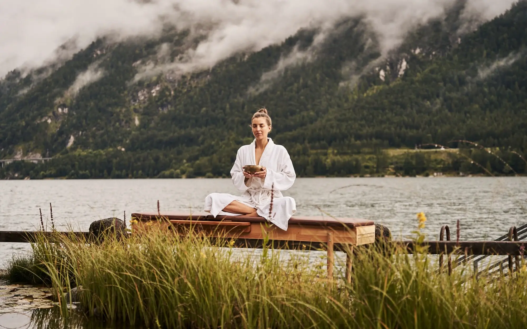 Woman sitting meditating on a jetty on the lakeshore.