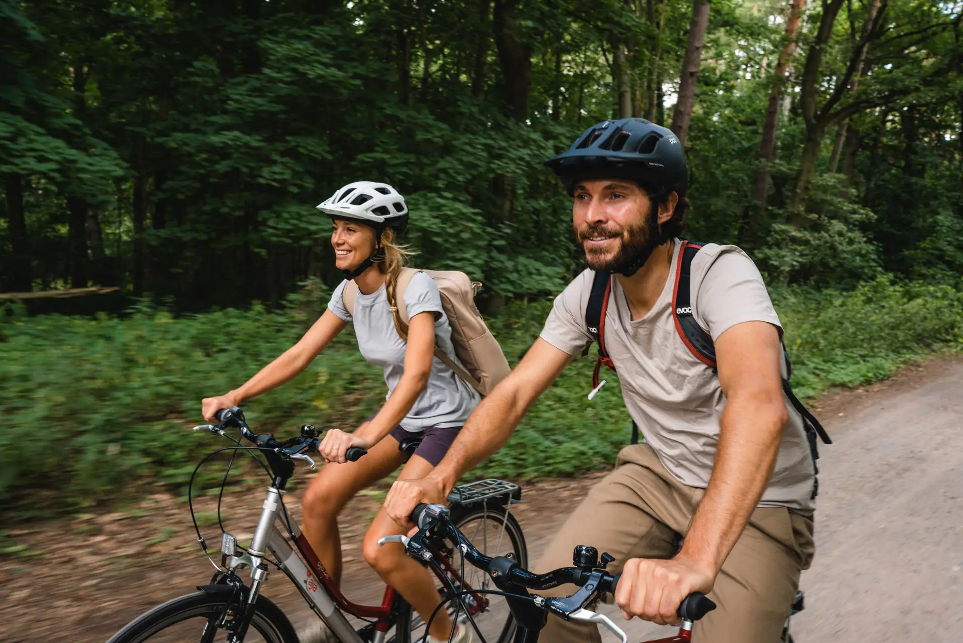 A man and a woman are cycling in the forest.