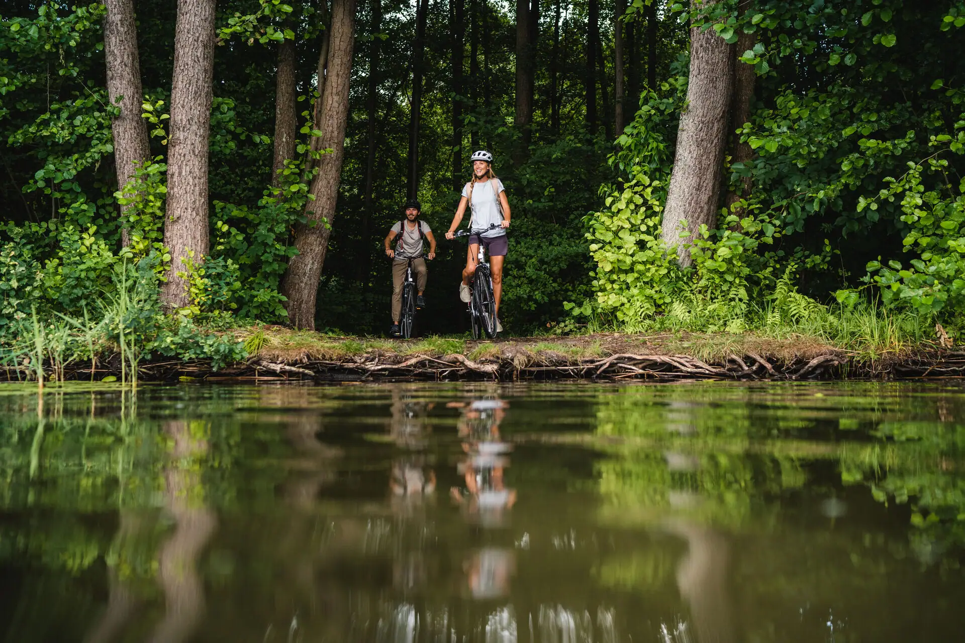 A man and a woman on bicycles on the bank of a body of water.