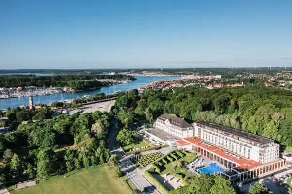 A-ROSA Travemünde Large building with a pool surrounded by trees and water.