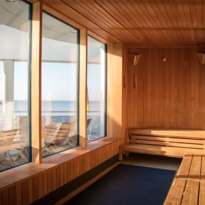 View from a wooden sauna out through three wide panoramic windows onto the sandy beach and the waters of the Baltic Sea.
