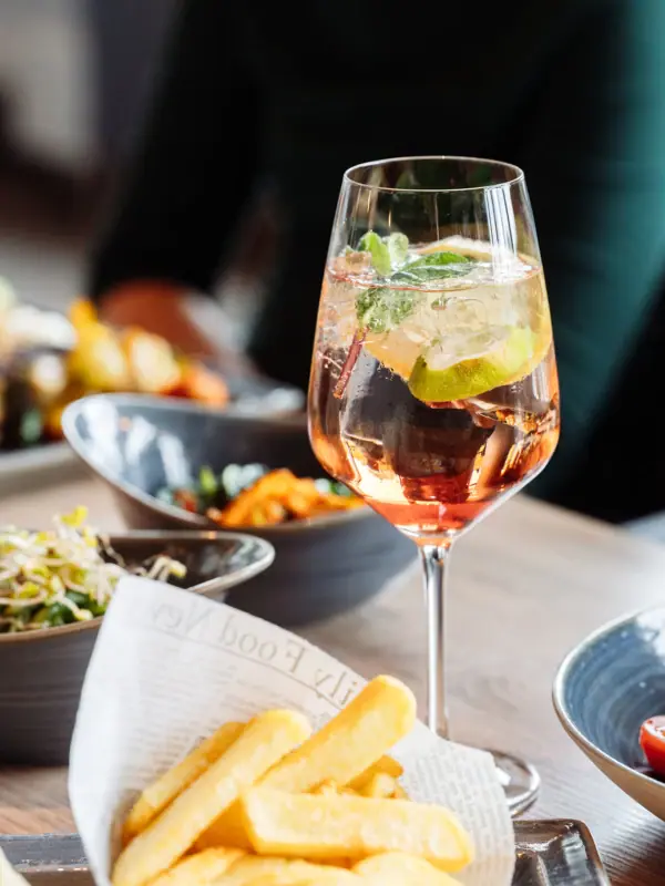 A drink and chips A glass of drink with a slice of lime and a mint leaf, served alongside a bowl of food.