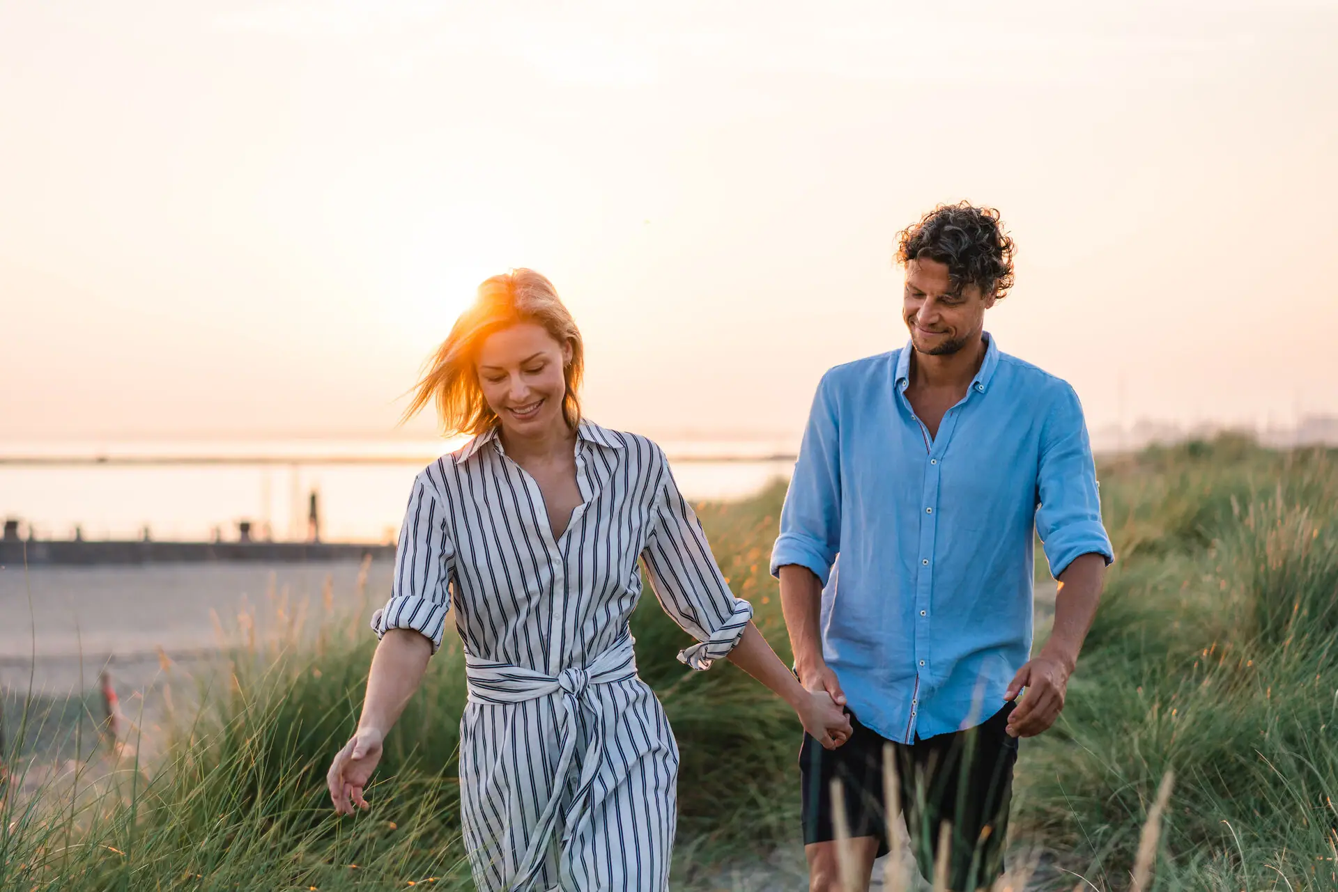 A man and a woman are holding hands and walking in a grassy area.