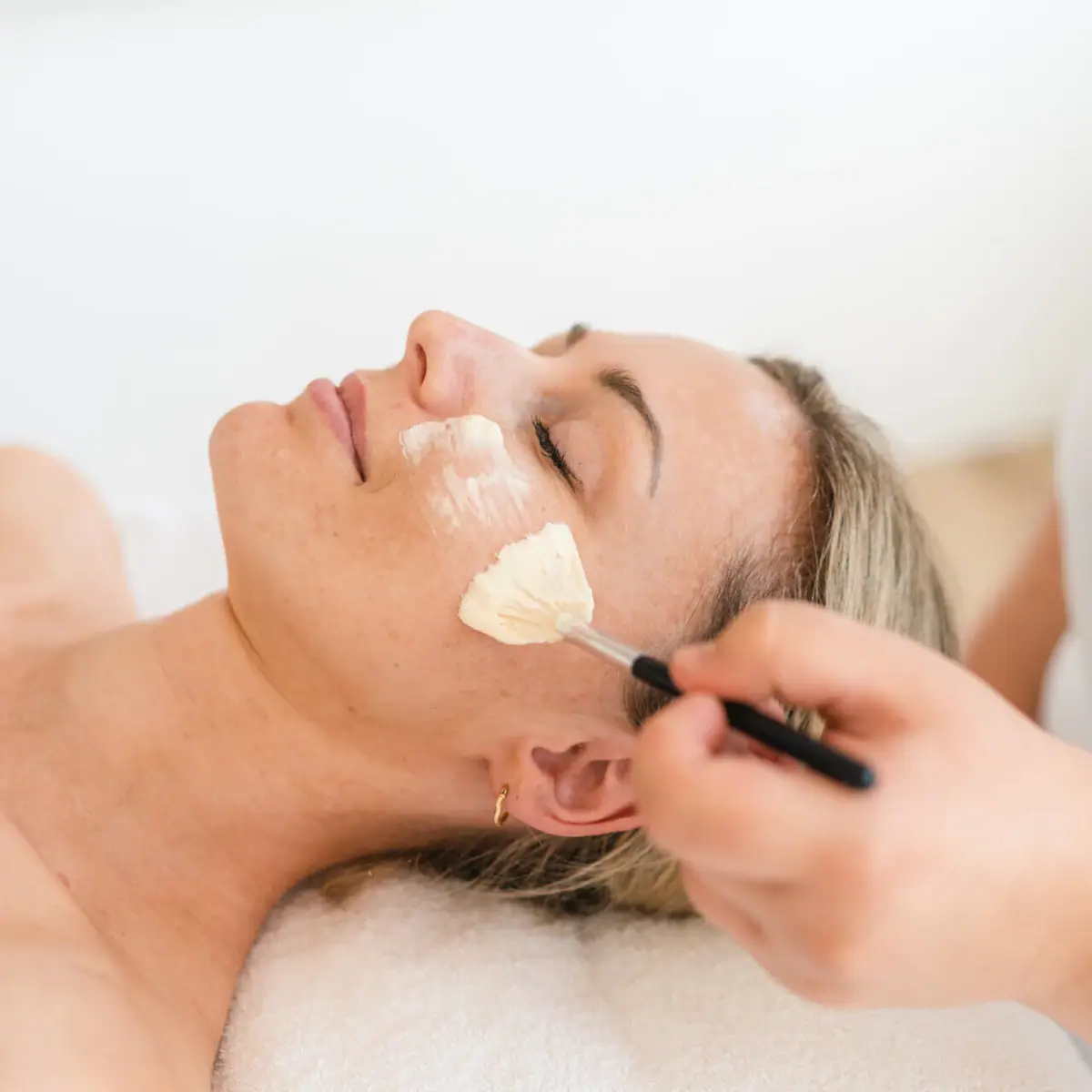Facial application A woman lies relaxed while a brush is passed over her face.