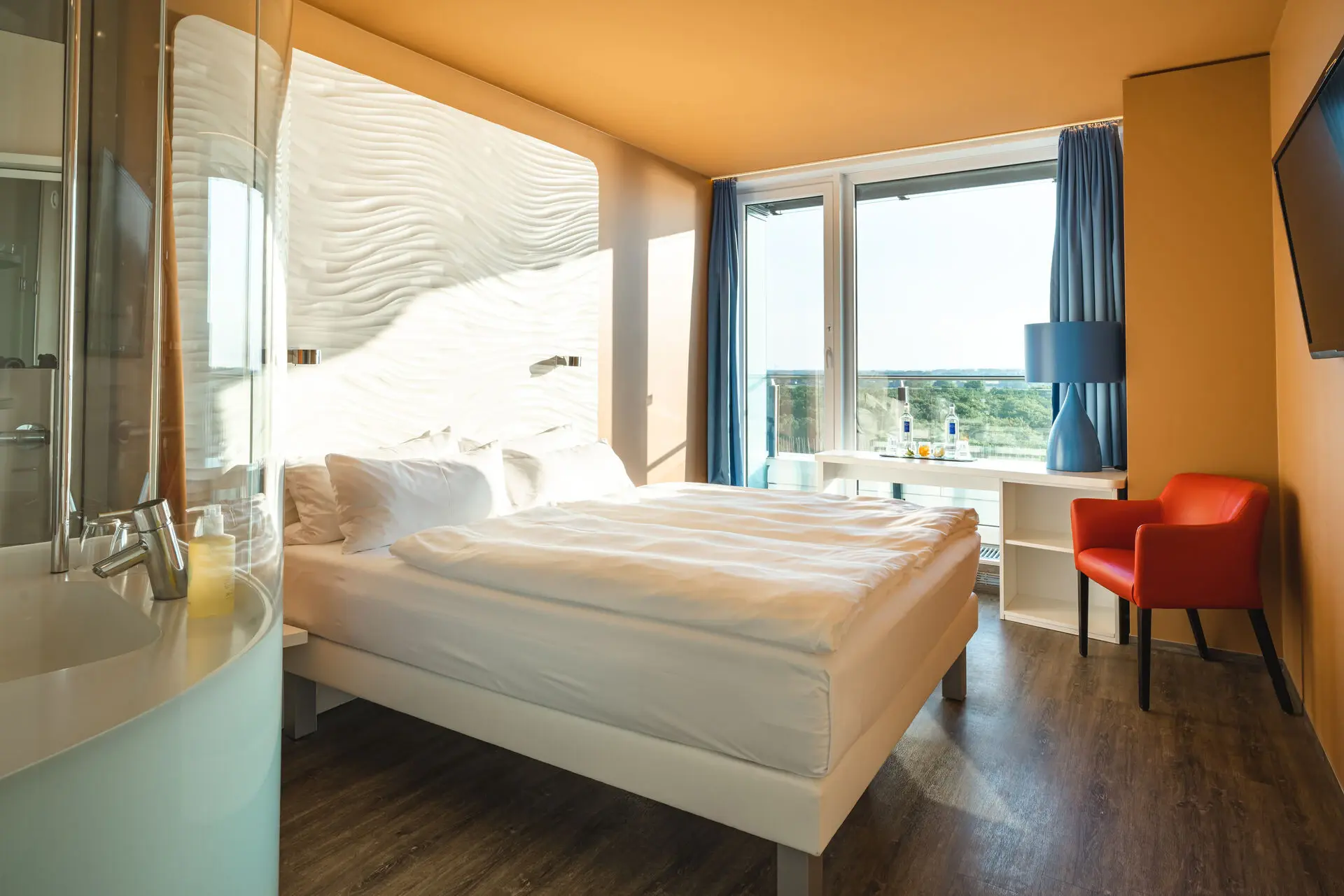 A room with a bed, a desk in front of the window and a red chair