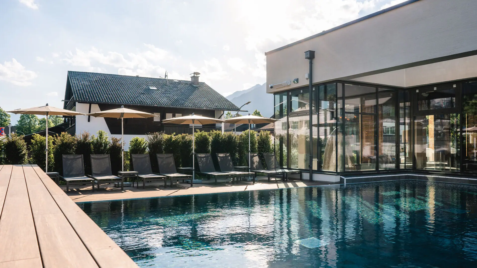 The outdoor pool at the aja Garmisch-Partenkirchen, with chairs and parasols in front of a building.