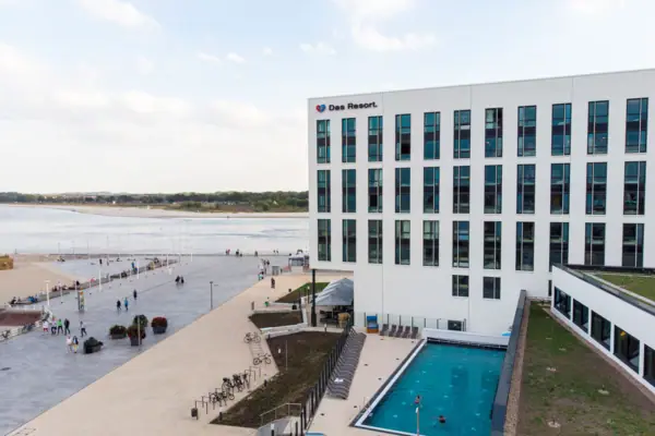 aja Hotel Travemünde A building with a swimming pool and people walking around.