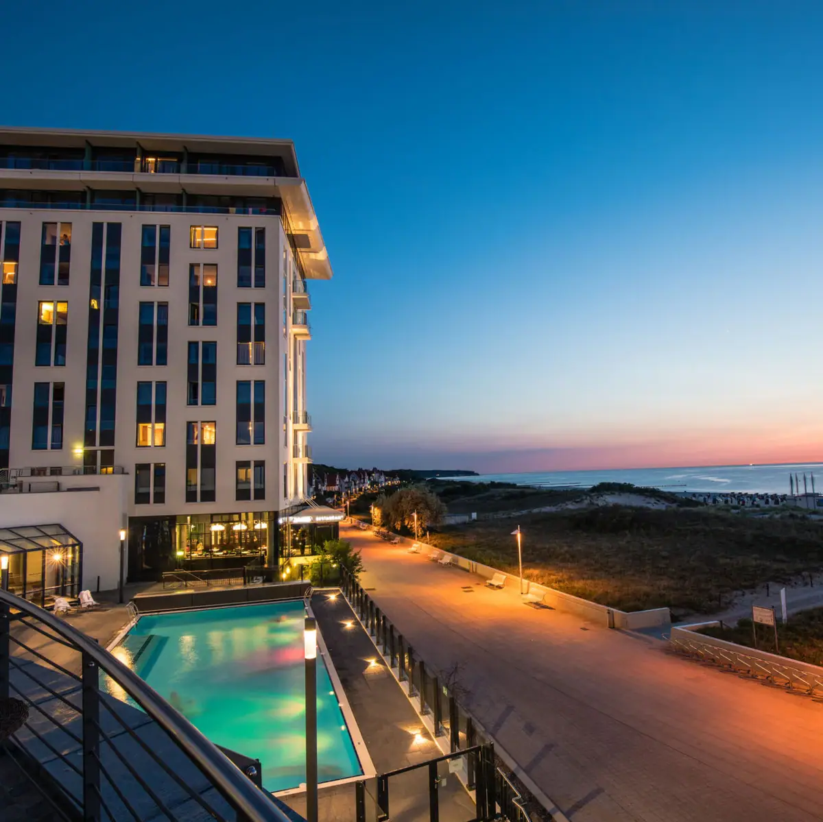 aja Warnemünde Building with pool and walkway by the sea at sunrise.