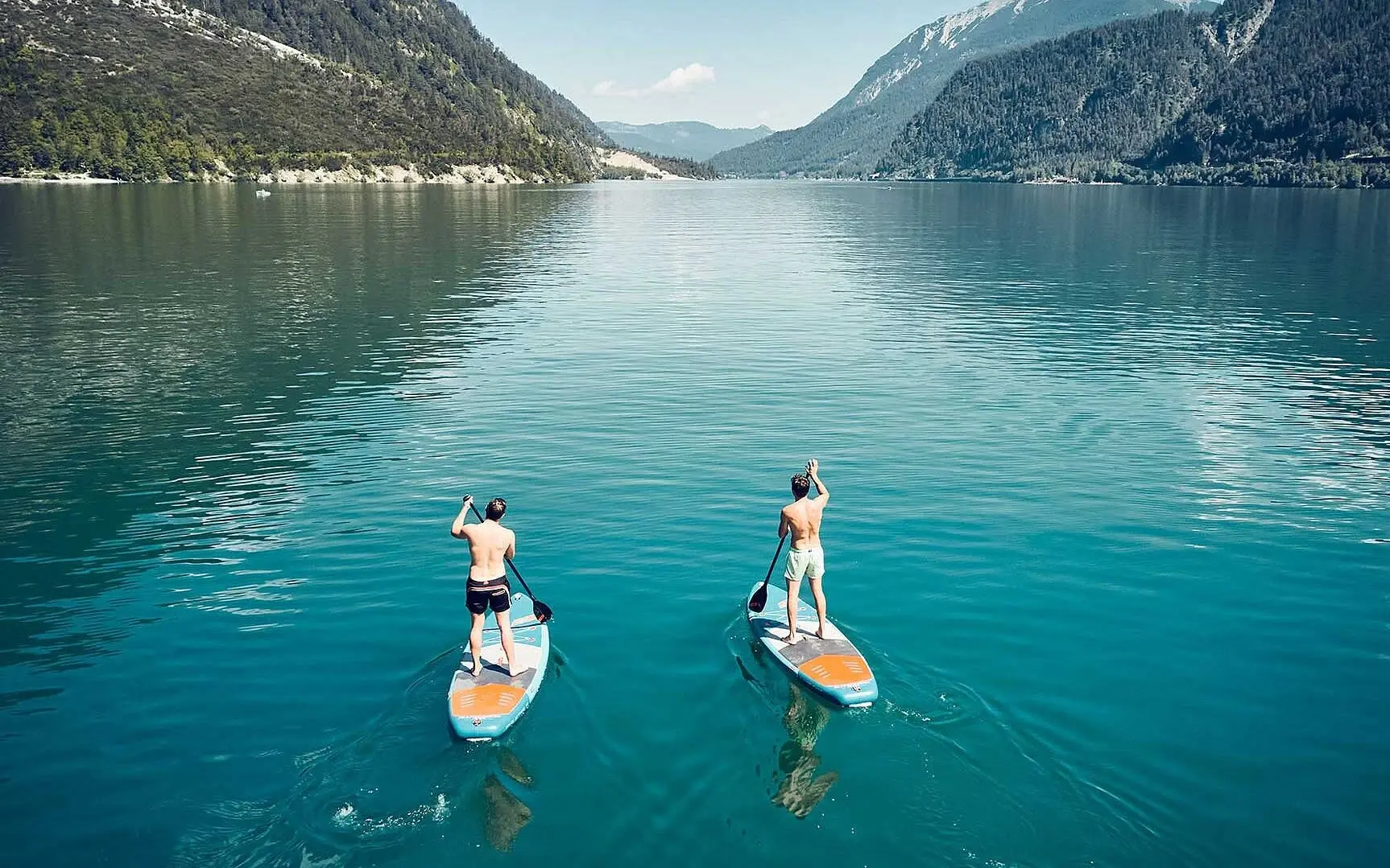 Two men on paddleboards on a lake with mountains in the background.