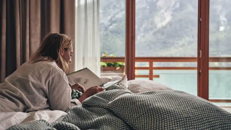 A woman lies on a bed and reads a book.
