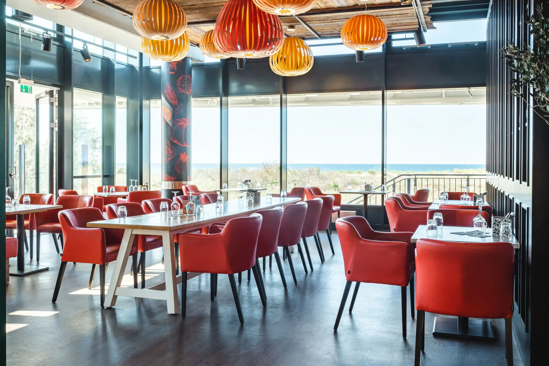 Restaurant with red chairs and tables and wide panoramic windows with a view of the sea in the background