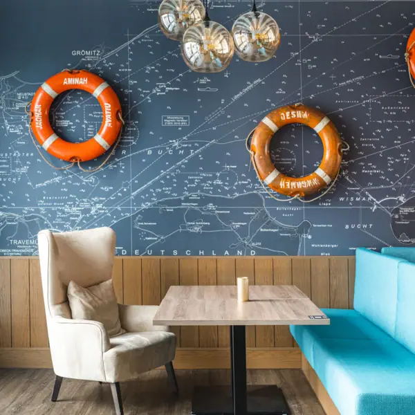 JEDERMANNS Restaurant, Grömitz A table and chairs, with a blue sofa and orange lifebuoys on the wall.
