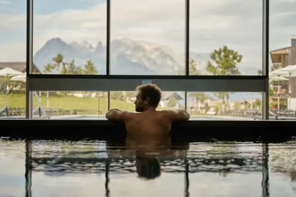 Man swimming in a pool with mountain and tree views.