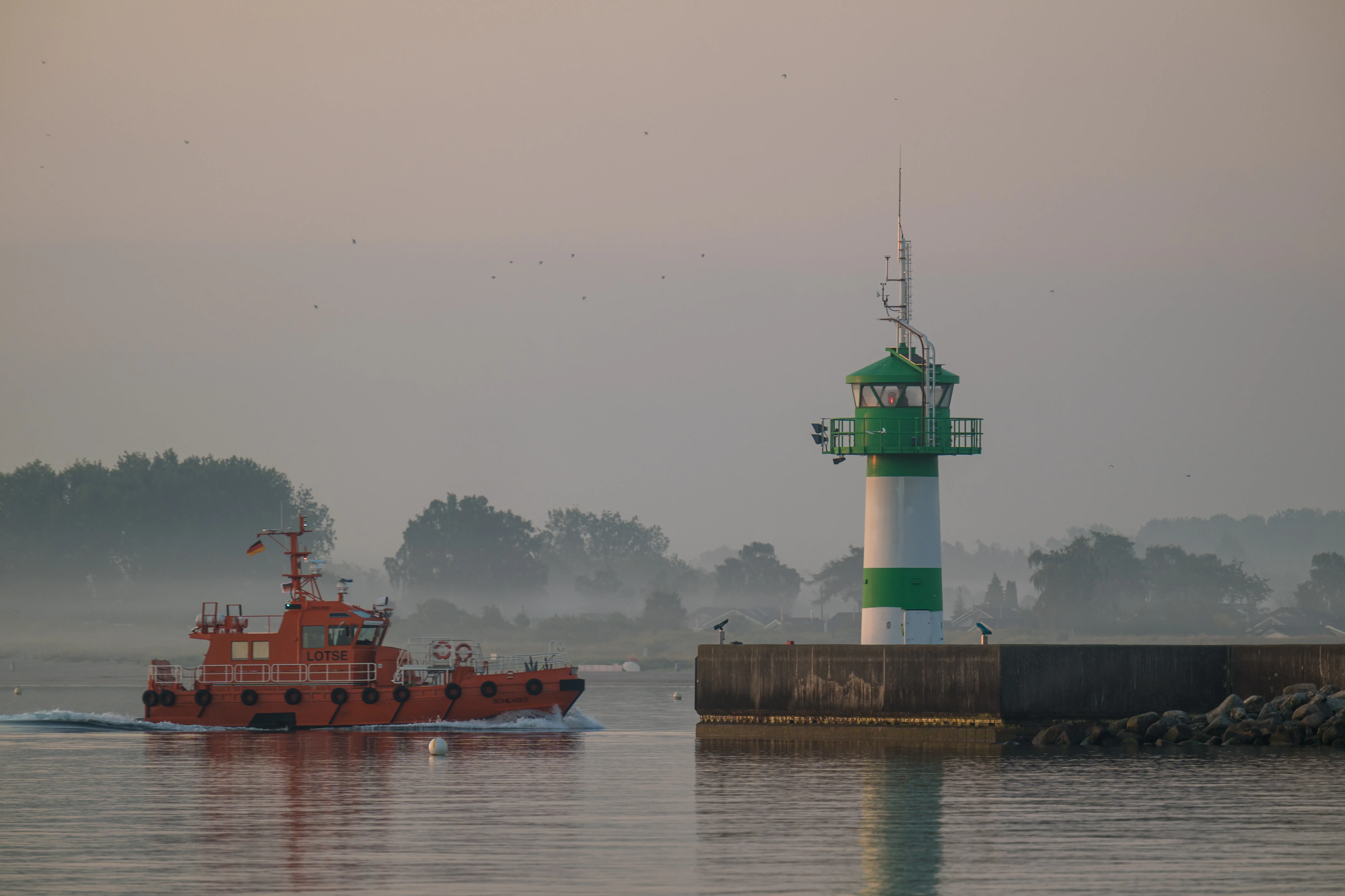 A boat on the water with a lighthouse in the background.