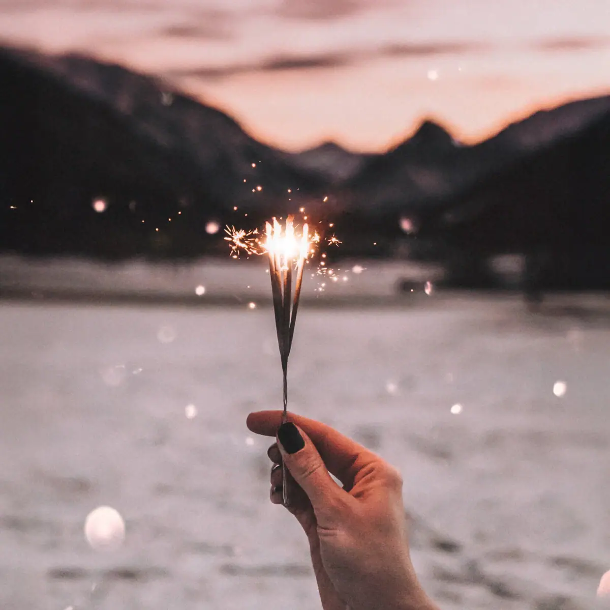 A hand holds a sparkler, the snow-covered mountain panorama can be seen in the background