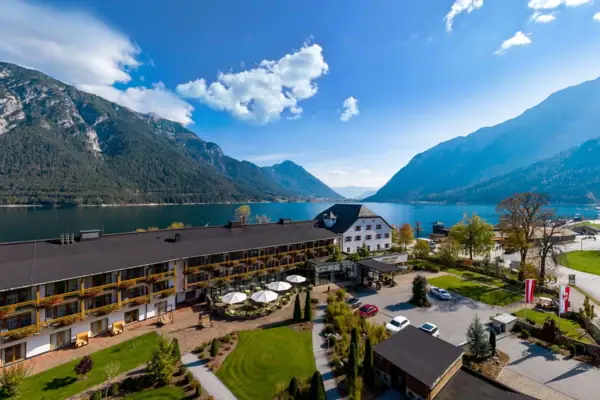 A building near a lake with clouds in the sky and trees in the foreground.