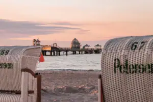 Ein Strandkorb am Strand mit einem Pier im Hintergrund.