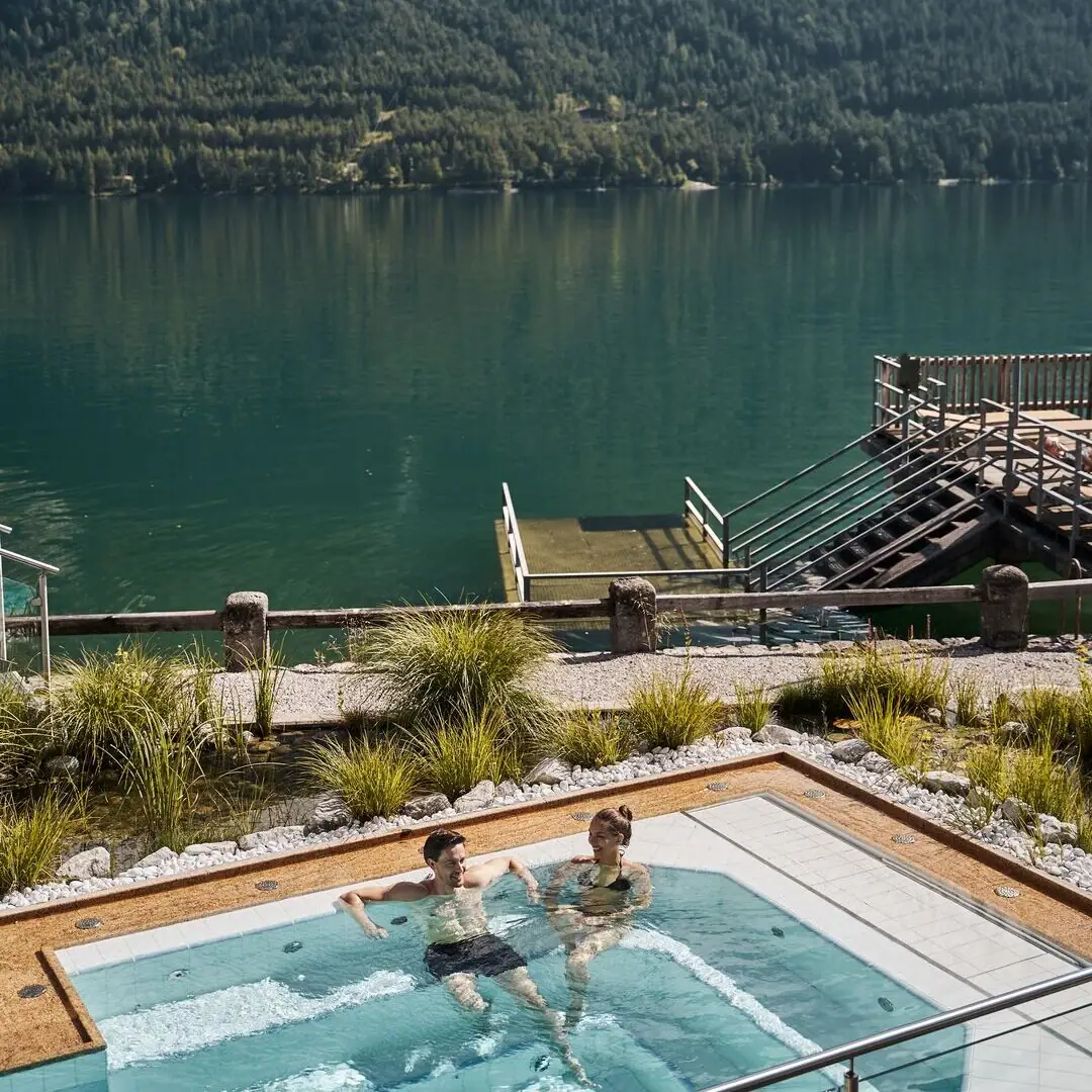 Whirlpool People in a swimming pool with a body of water and mountains in the background