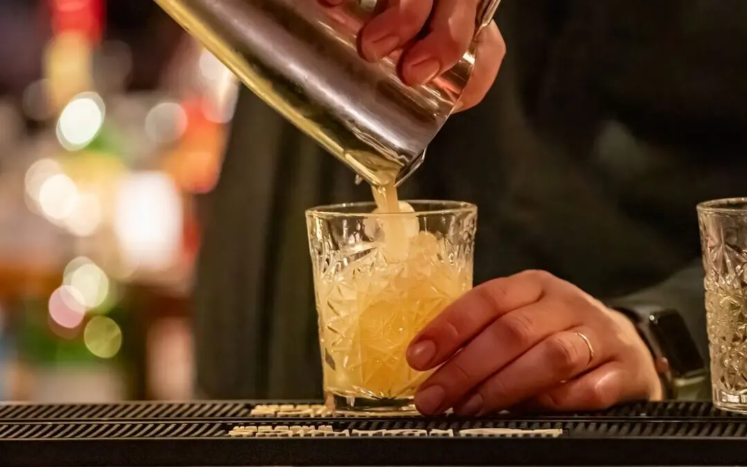 Bartender pours a cocktail into a glass.