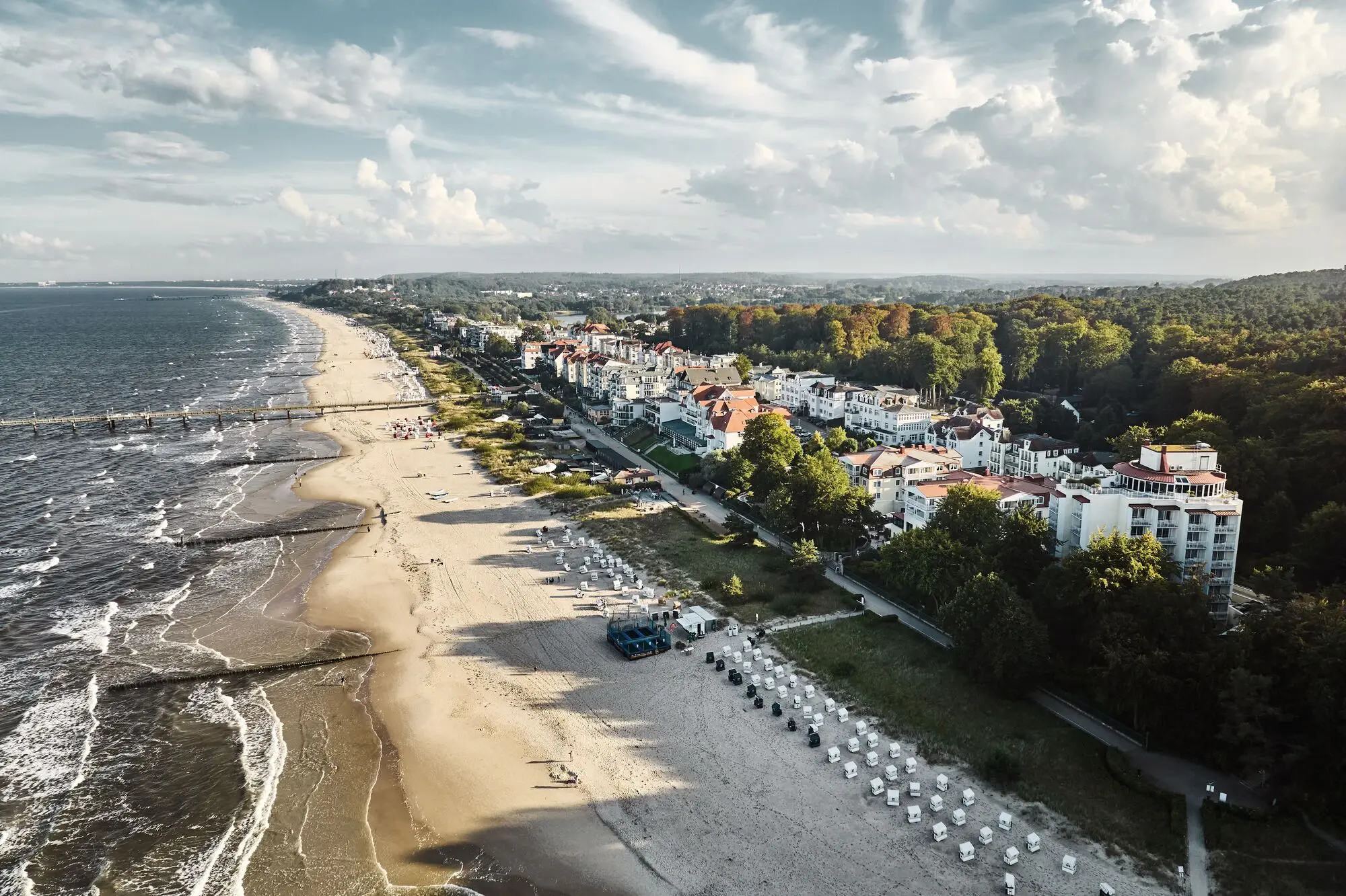 Beach with buildings and trees under a cloudy sky.