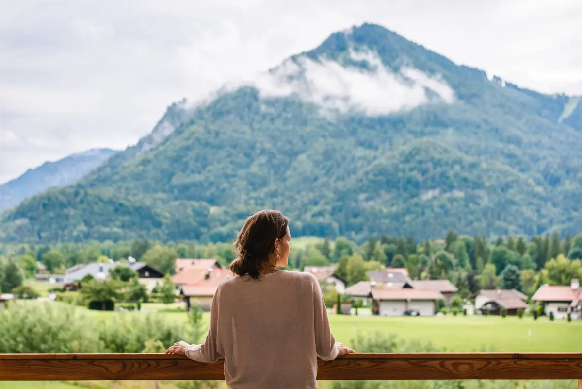 View from the aja Ruhpolding A woman is standing on a balcony, looking out at a range of mountains.
