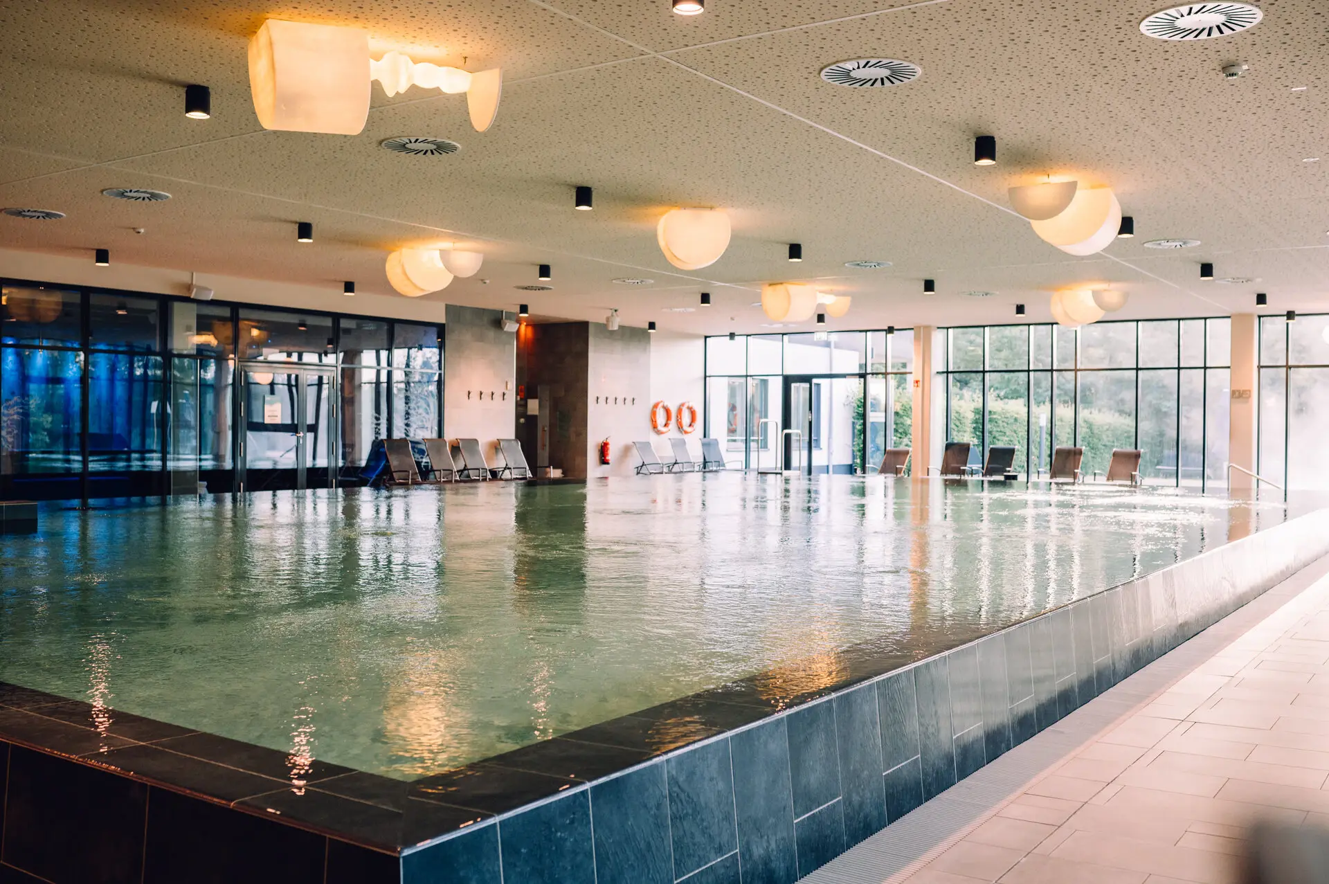 Large indoor pool with loungers with ceiling lights