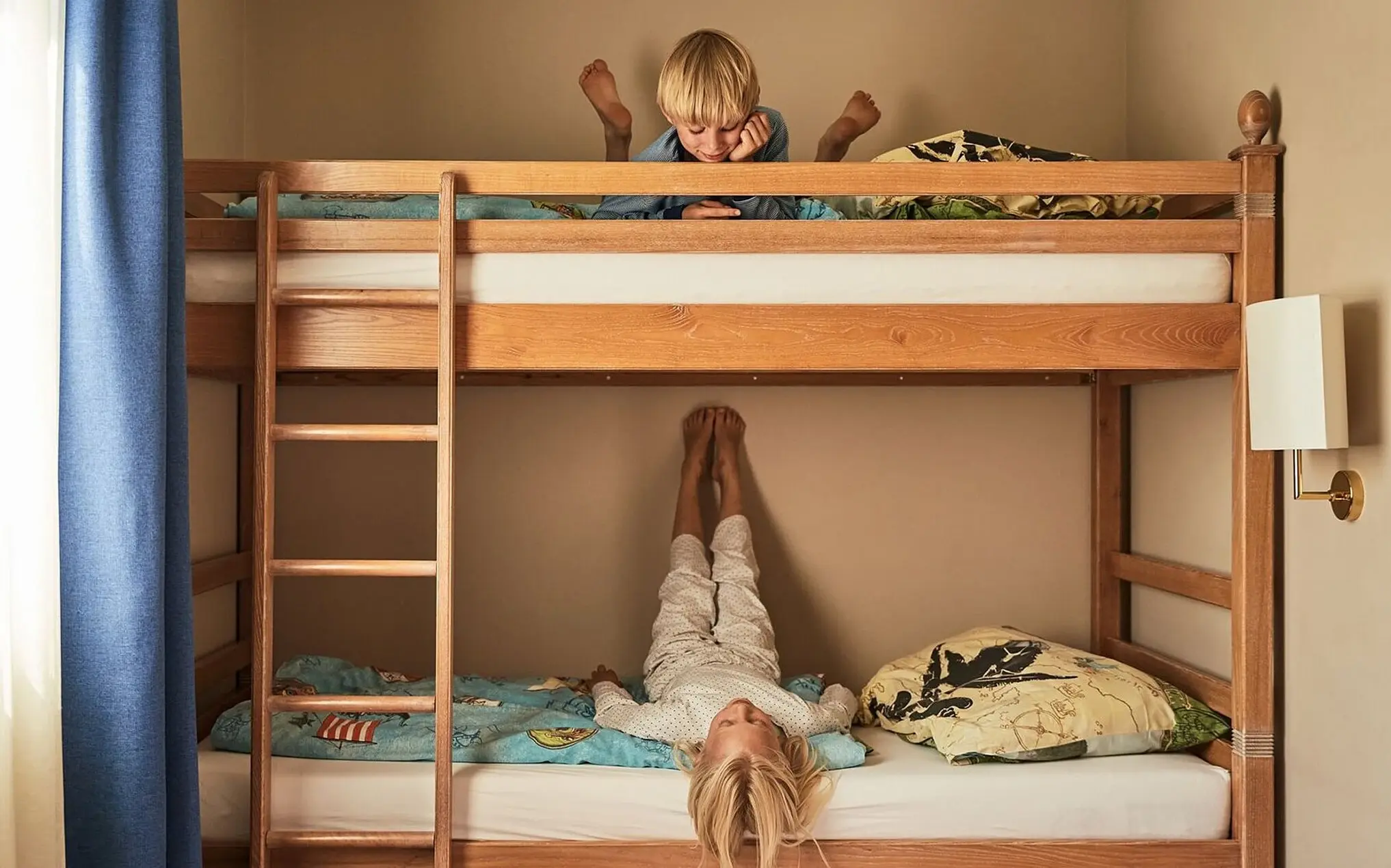 A boy is lying on top of a bunk bed next to a ladder.