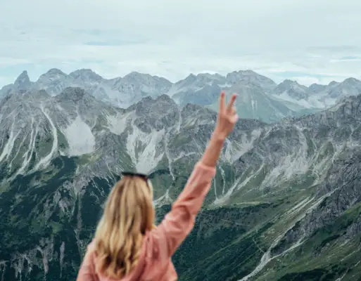 Active with aja  A woman stands on a mountain and raises her hand.