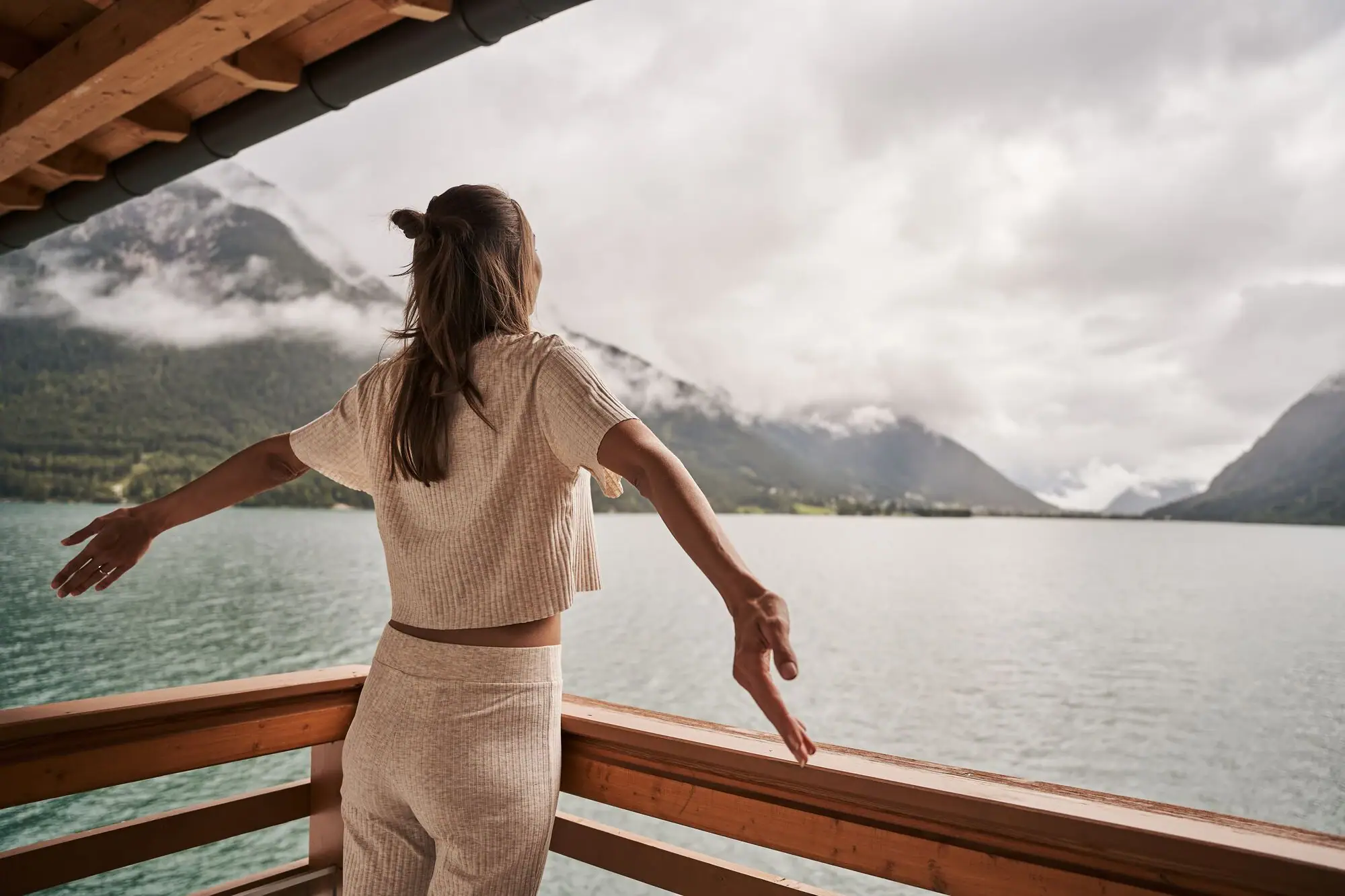 Woman on the balcony at Lake Achensee A woman stands on a balcony overlooking a body of water.