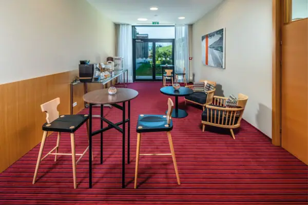 A room with a red carpet, scattered seating, a coffee bar and a large patio door at the back. 