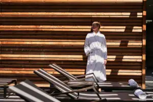 Eine Frau in einem weißen Bademantel steht vor einer Holzwand.