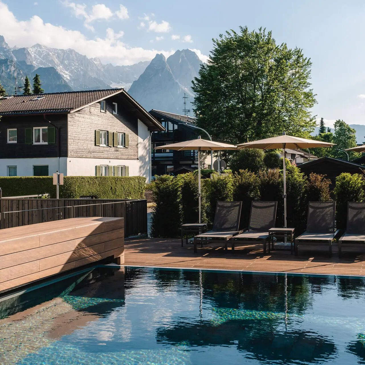 Outdoor pool aja Garmisch-Partenkirchen A pool with chairs and parasols next to a house.