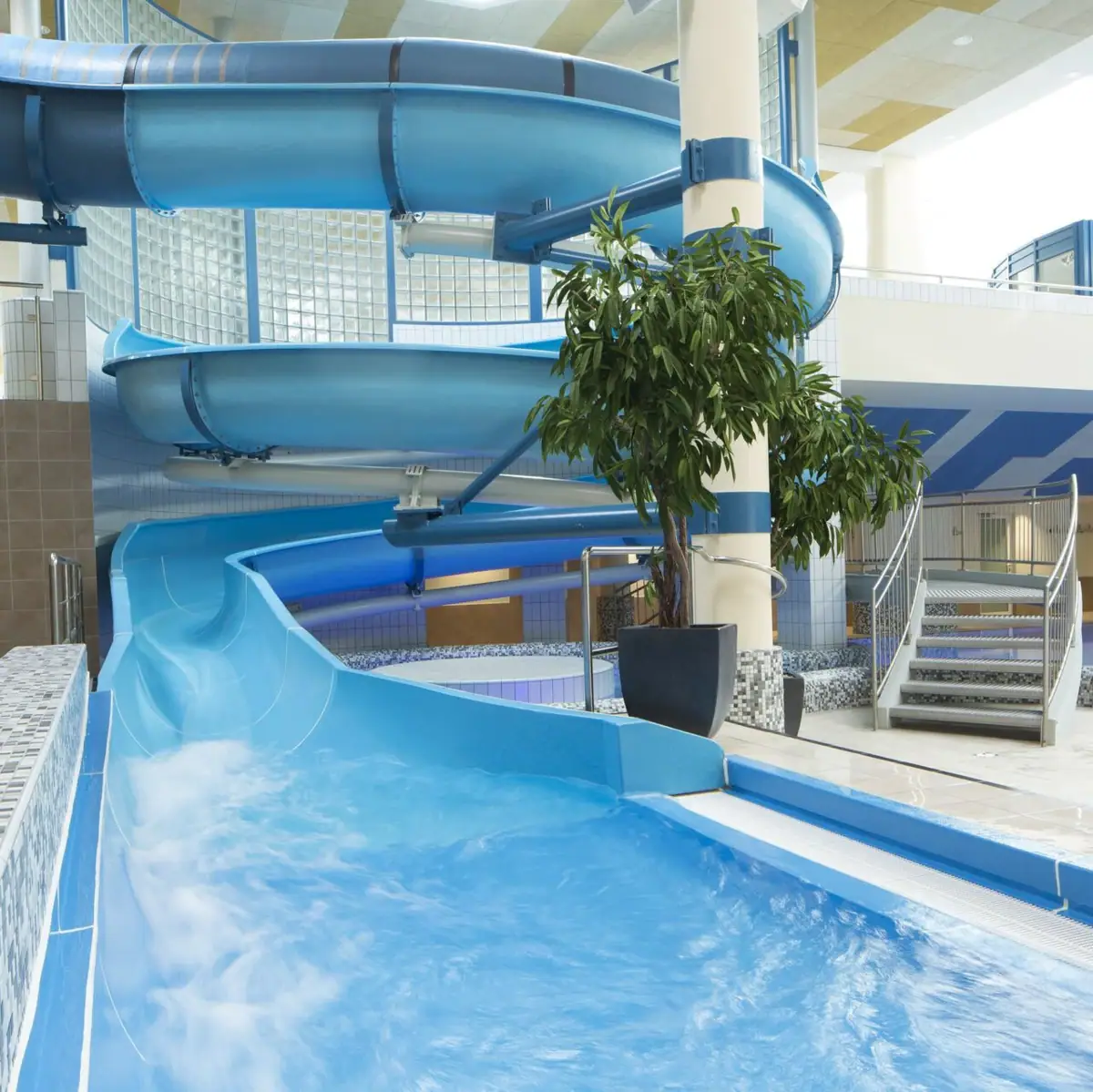 Water slide in a building with adjoining swimming pool.