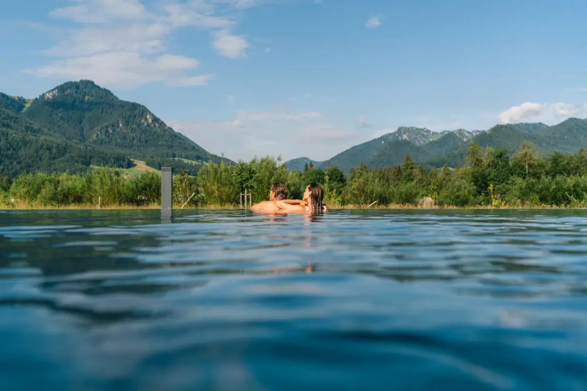 A couple swim in a pool against a mountain backdrop.