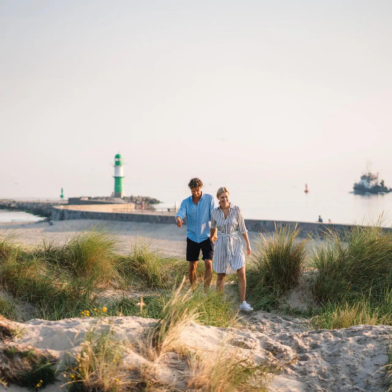 Experiences at aja Warnemünde A man and a woman walk along the beach.