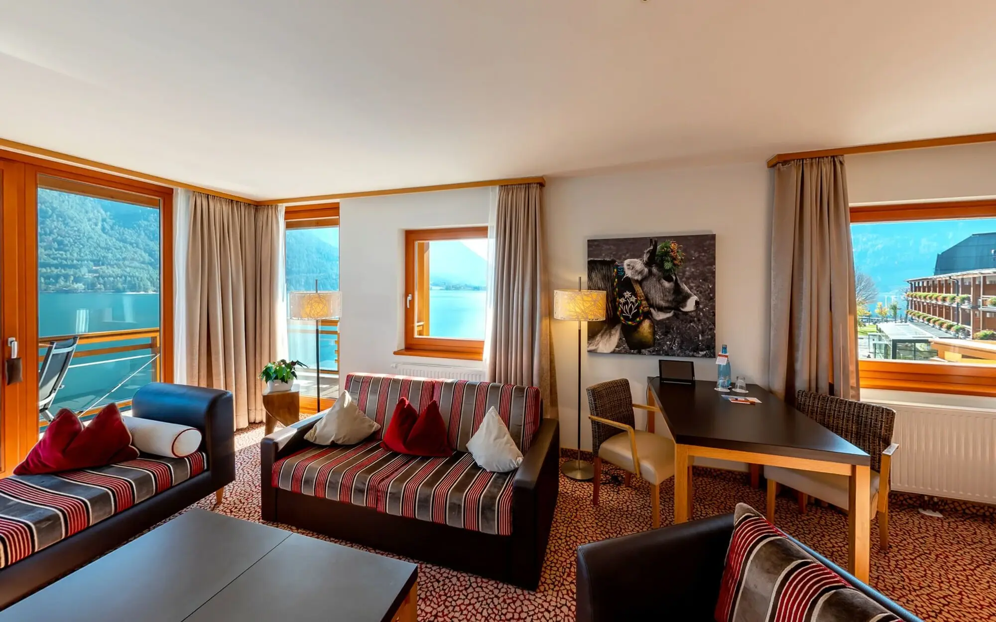 Interior of a living room with sofas, armchairs and a balcony with a view of Lake Achensee.