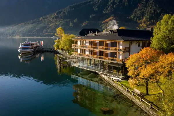 Building by the water with trees and mountains in the background.