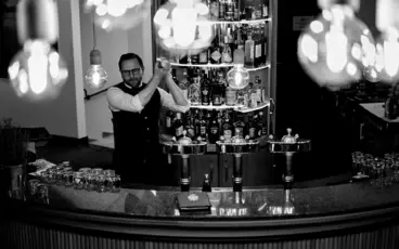 A man stands behind a bar and mixes a cocktail, black and white shot.