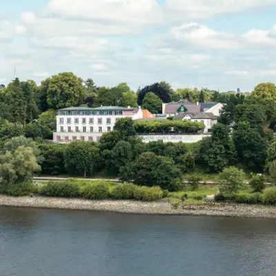 A building near a body of water with trees and clouds in the sky.