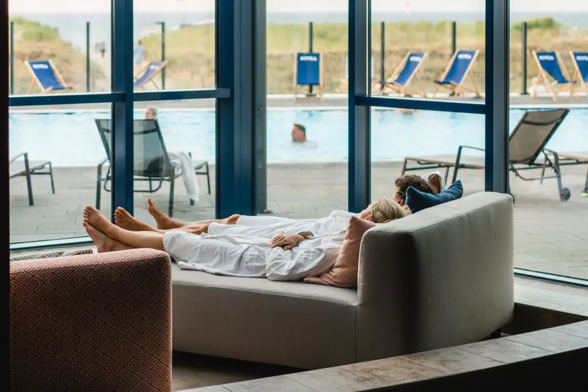 Relaxation area at the aja Warnemünde A woman lies on a couch next to a pool.