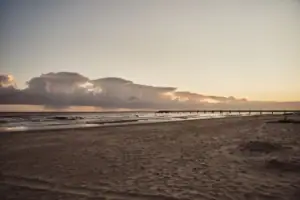 Ein Strand mit einem Pier und Wasser im Vordergrund.