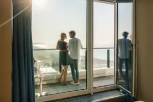 Suite at the aja Warnemünde A man and a woman stand on a balcony overlooking a beach.