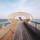 Person stands on a wooden footbridge by the water.