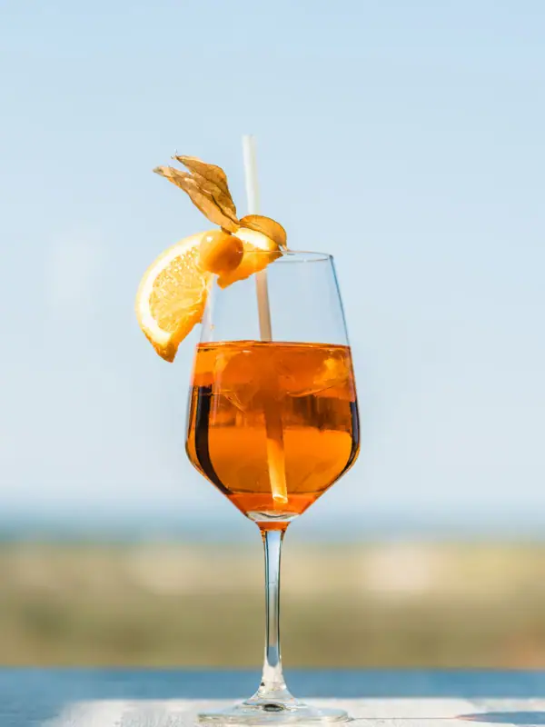 A glass with orange-coloured liquid, a straw and a slice of orange on top.