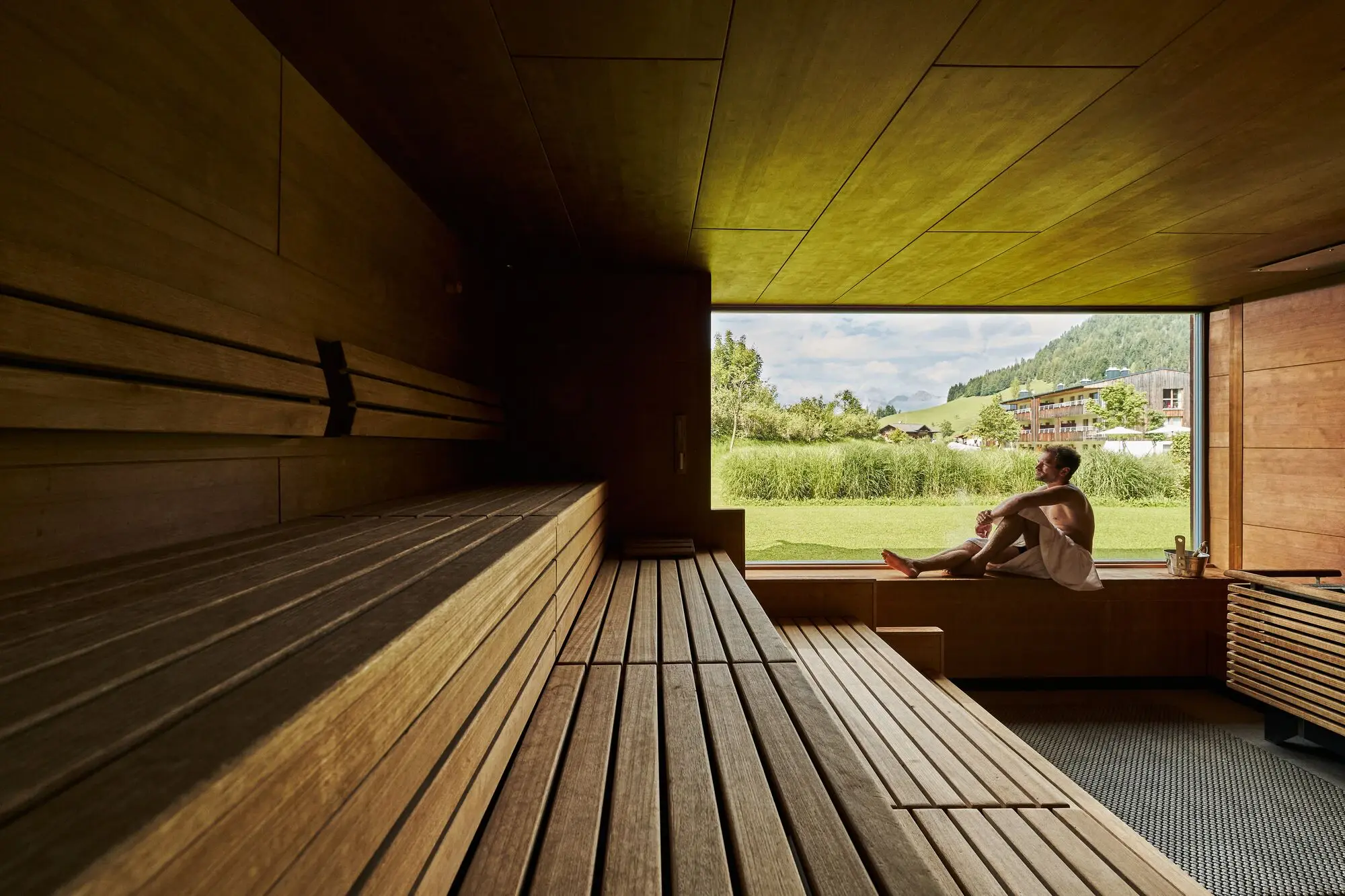 Man sitting on a bench in a sauna with a window.