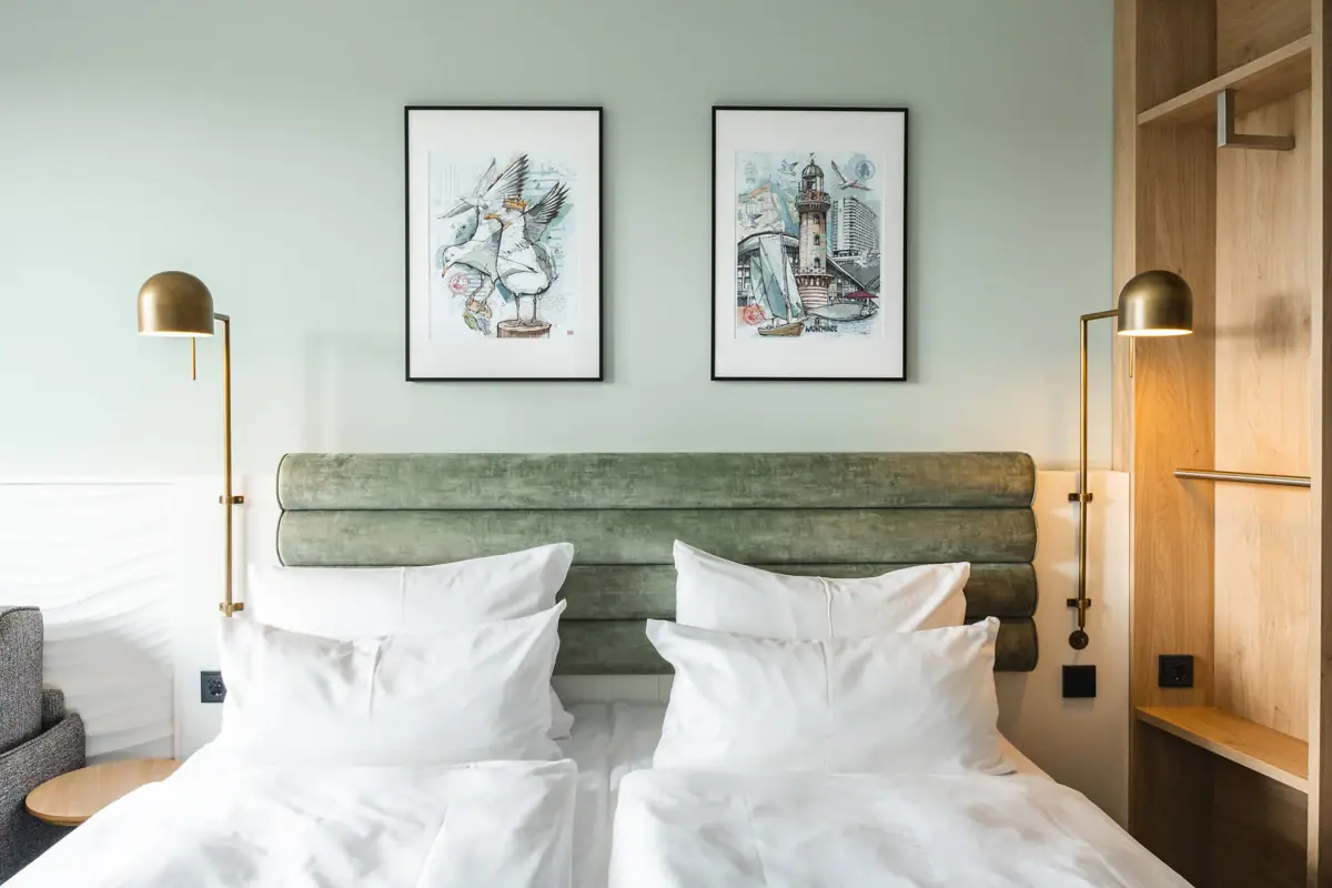 Bed with white cushions and green headboard, flanked by two lamps.