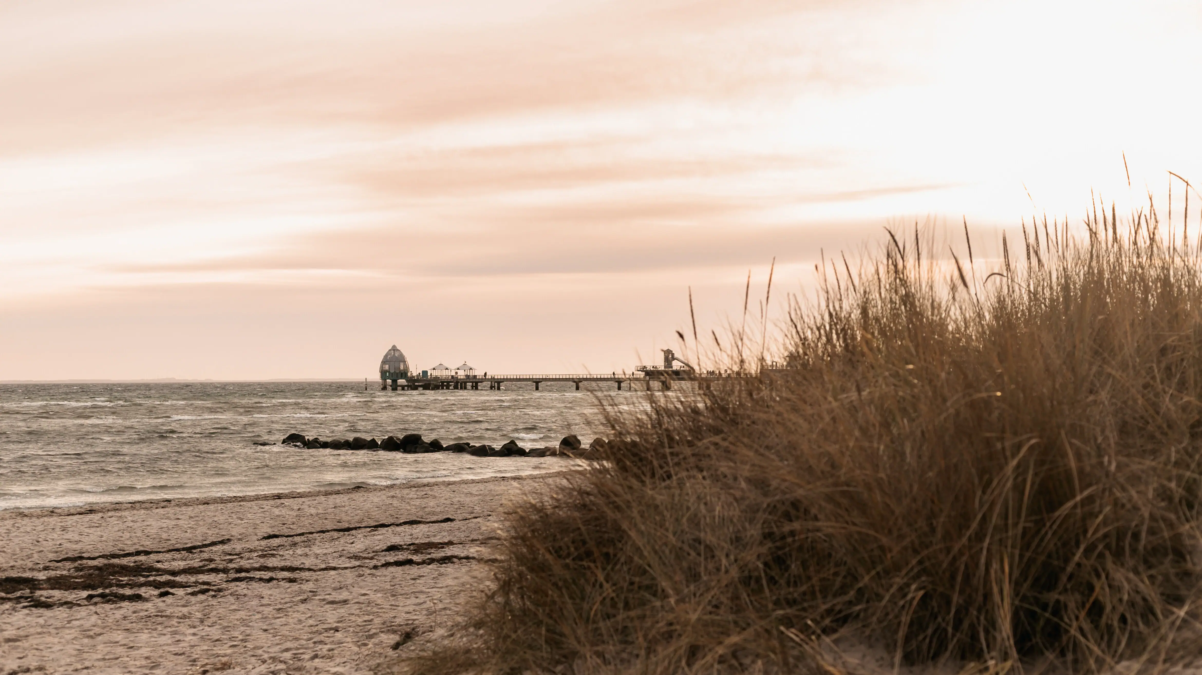 A beach with a jetty and grass in the foreground.